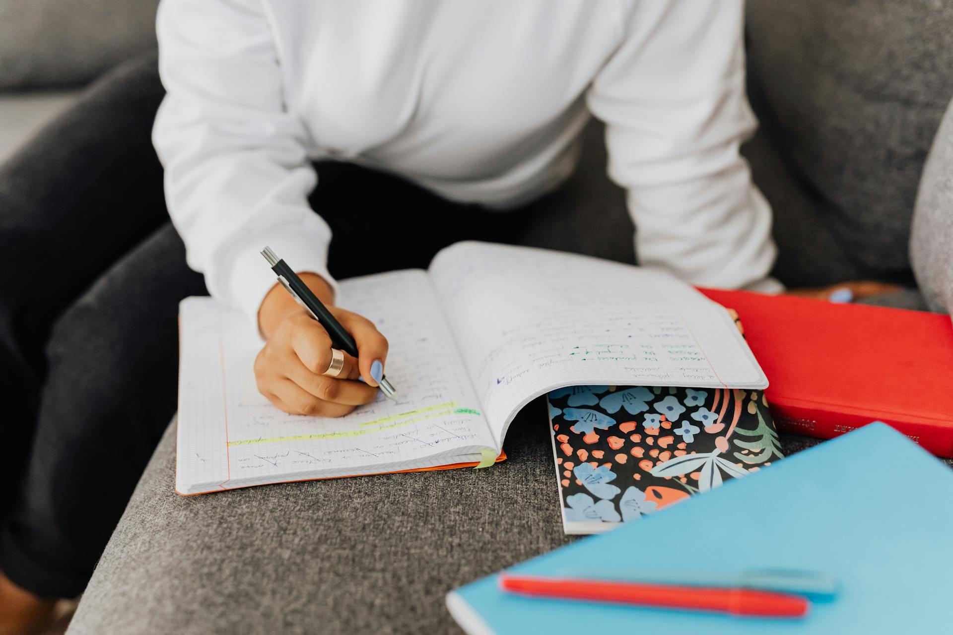 A student writing notes in a cozy home setting, surrounded by colorful notebooks.