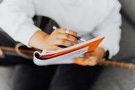 Person in White Long Sleeves Shirt Writing on a Notebook