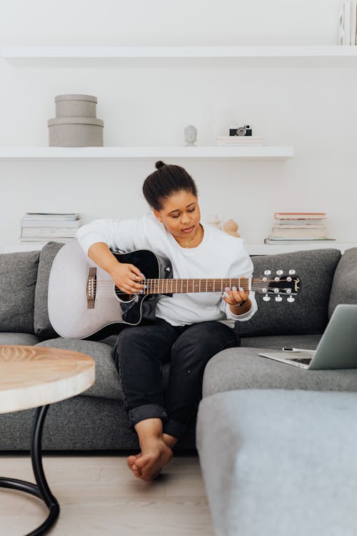 A Woman in White Sweater Sitting on the Couch while Playing Guitar