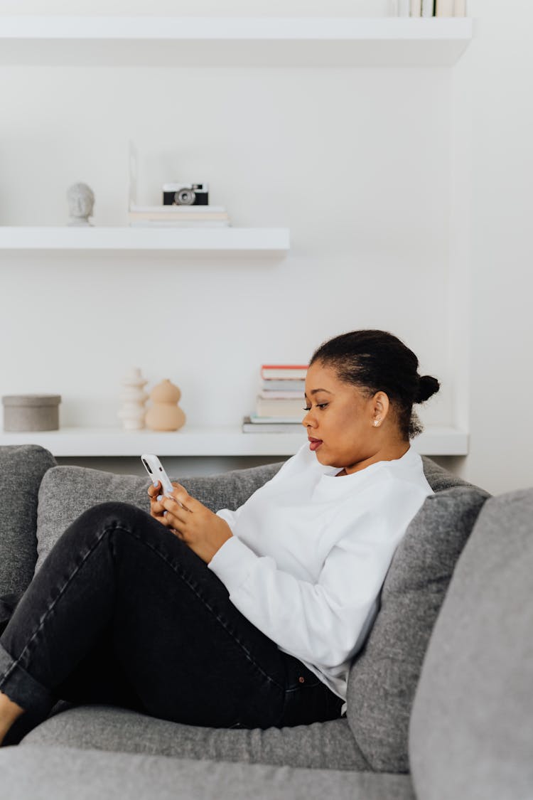 A Woman Leaning On The Couch While Using Her Phone