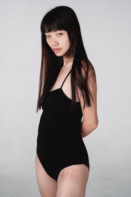 Attractive Asian woman in bodysuit standing in light studio