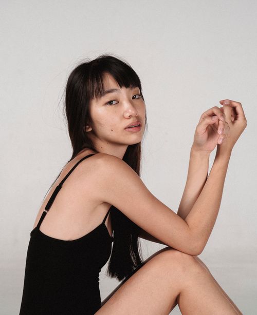 Free Side view young calm Asian female model wearing black bodysuit sitting against white background in studio and looking at camera Stock Photo
