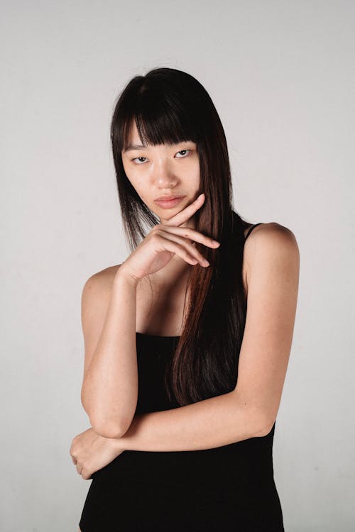 Free Gorgeous Asian woman touching chin gracefully in light studio Stock Photo