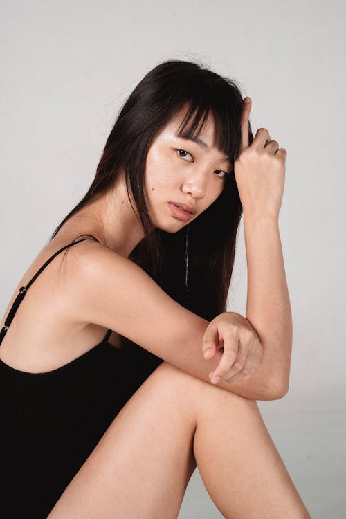 Attractive Asian woman sitting in light studio and touching head