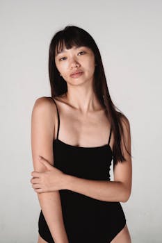 Portrait of a young Asian woman in a black bodysuit with a calm expression on a white background.