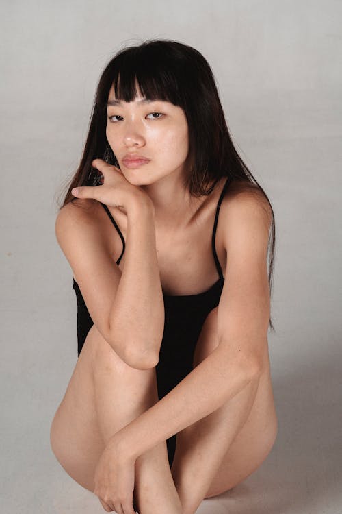 Gorgeous Asian woman in bodysuit sitting on floor gracefully