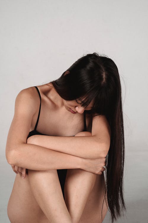 Alluring young Asian female embracing knees in studio