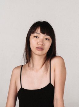 一位深色头发、身着黑色上衣的年轻少数族裔女模特，在灰色背景下冷静地注视着镜头