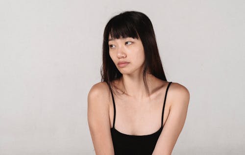 Melancholic Asian woman near wall on gray background