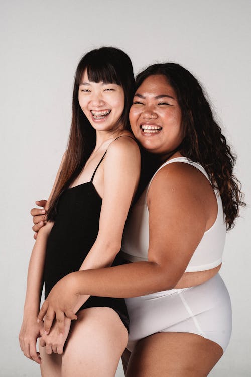 Laughing young Asian girlfriends in underwear cuddling in studio