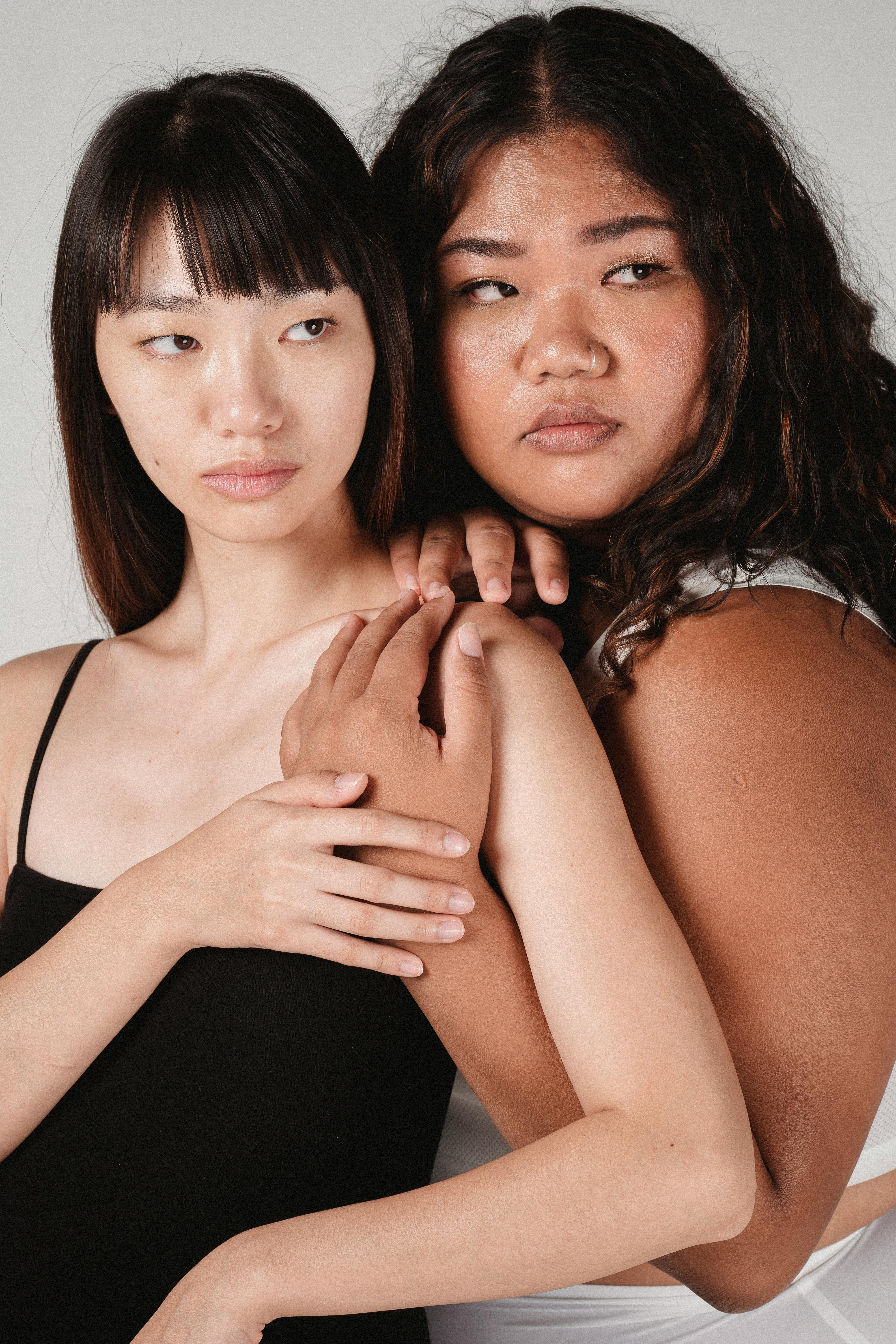 graceful young ethnic ladies hugging and looking away