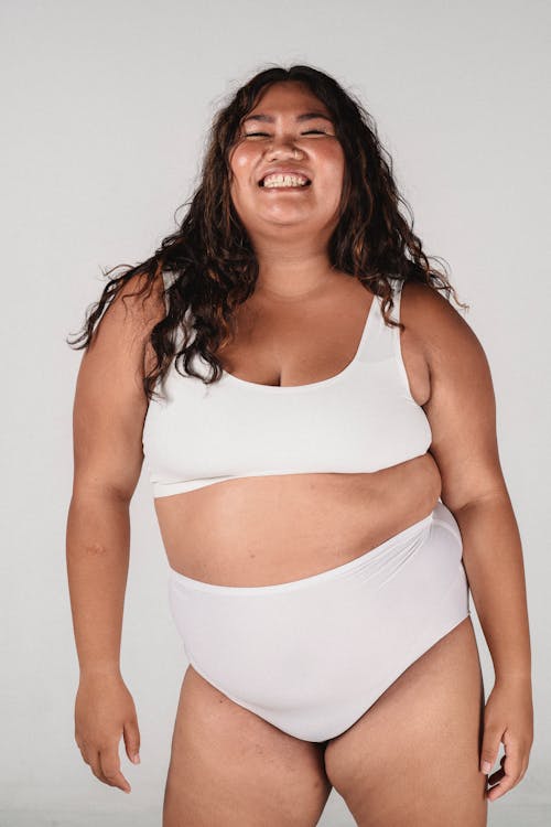 Plus size delighted Asian female with long hair in underwear on white background