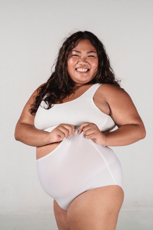 Free Overweight cheerful Asian female with long hair smiling and pulling pants on white background Stock Photo