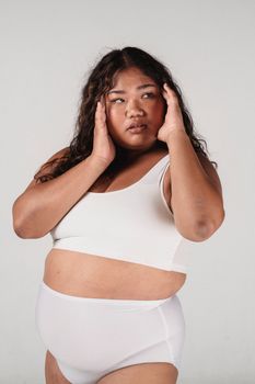 Young overweight Asian female with long hair touching face and looking away on white background