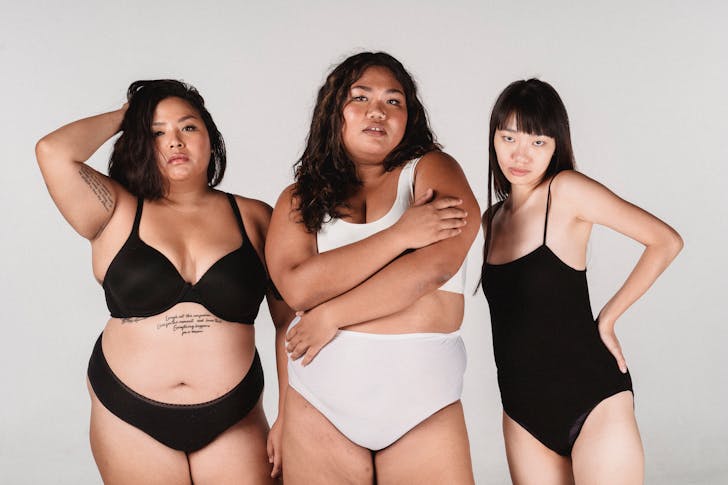 Group of Asian plus size and slender women in underwear looking at camera on white background
