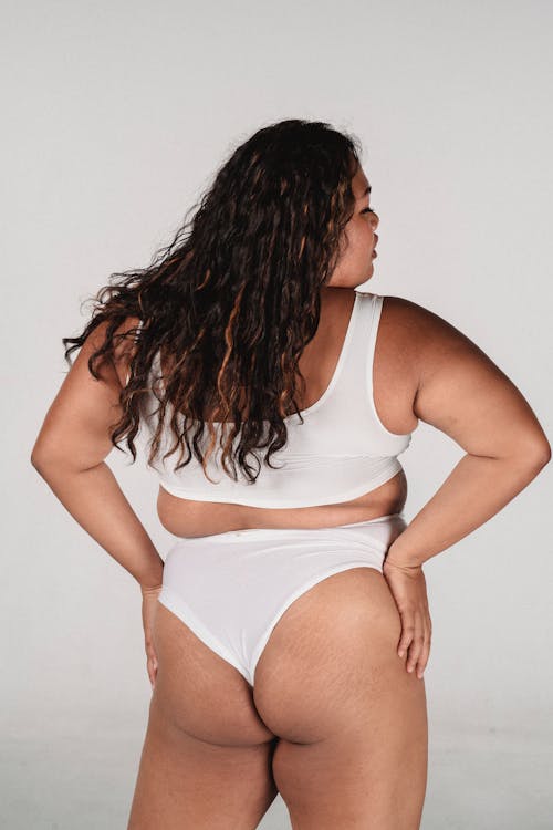 Back view of overweight woman with long brown hair in casual underwear standing against gray background