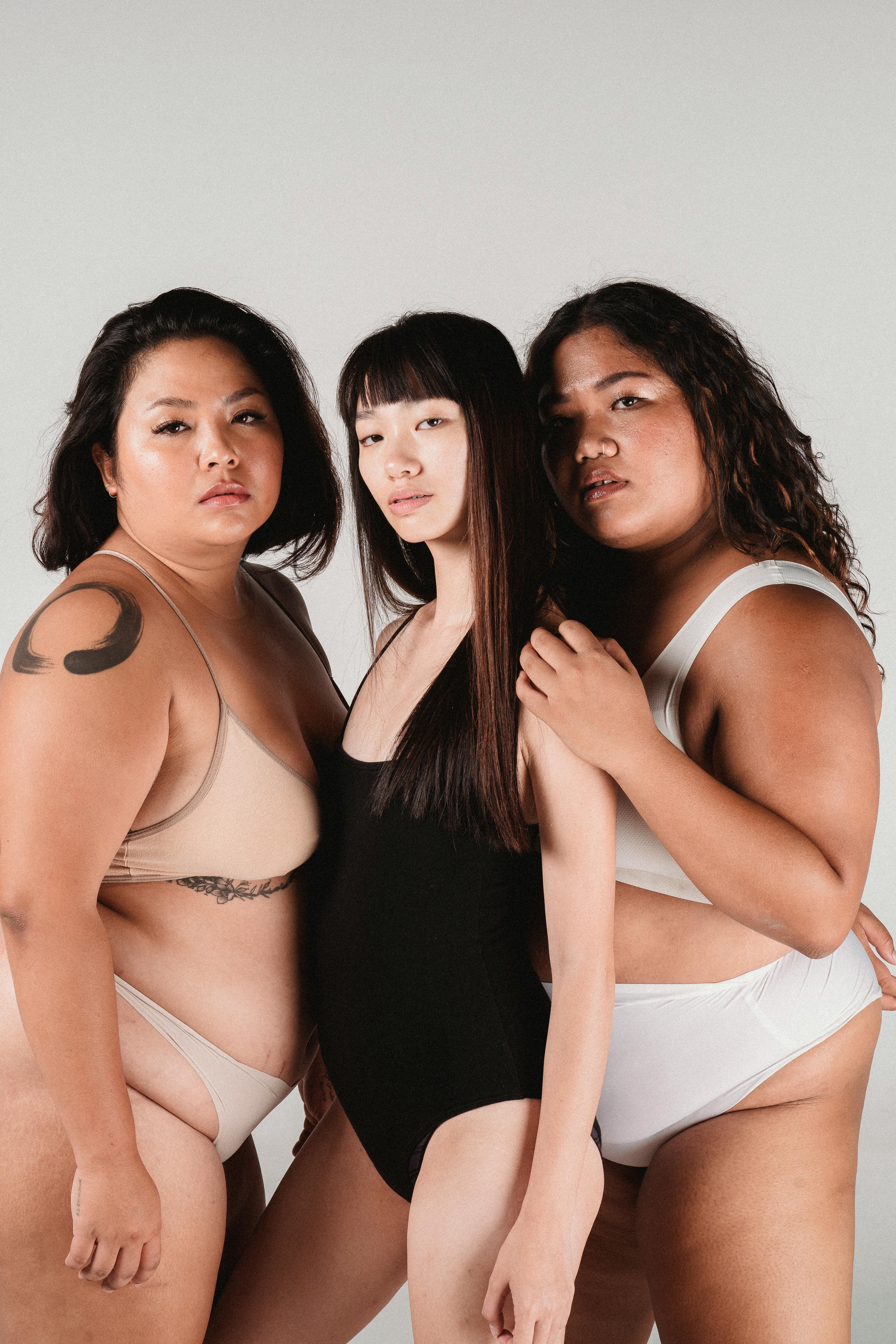 Side view of confident Asian models with brown hair in underwear standing close to each other against gray background