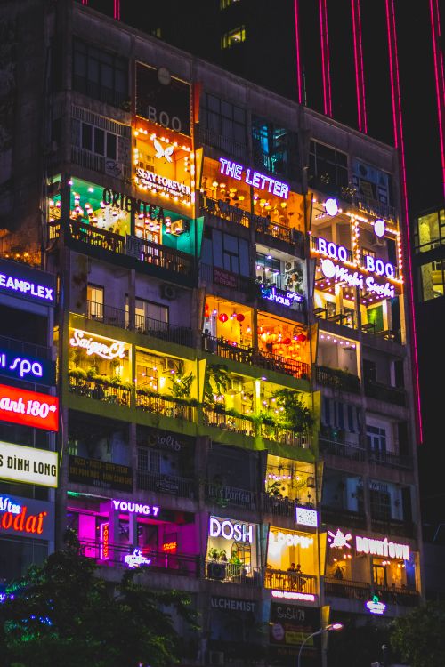 Free Vibrant urban nightlife scene featuring neon signs and illuminated windows on a multi-story building. Stock Photo