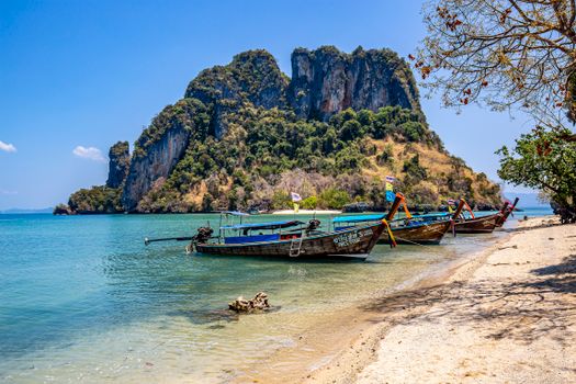 Idyllic Thai beach scene with fishing boats and rock formations under a clear blue sky.