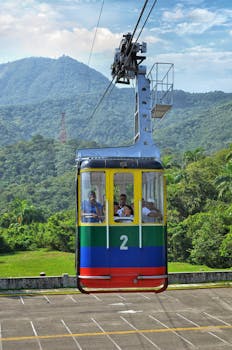 A vibrant cable car carrying passengers amidst lush green mountains on a sunny day.