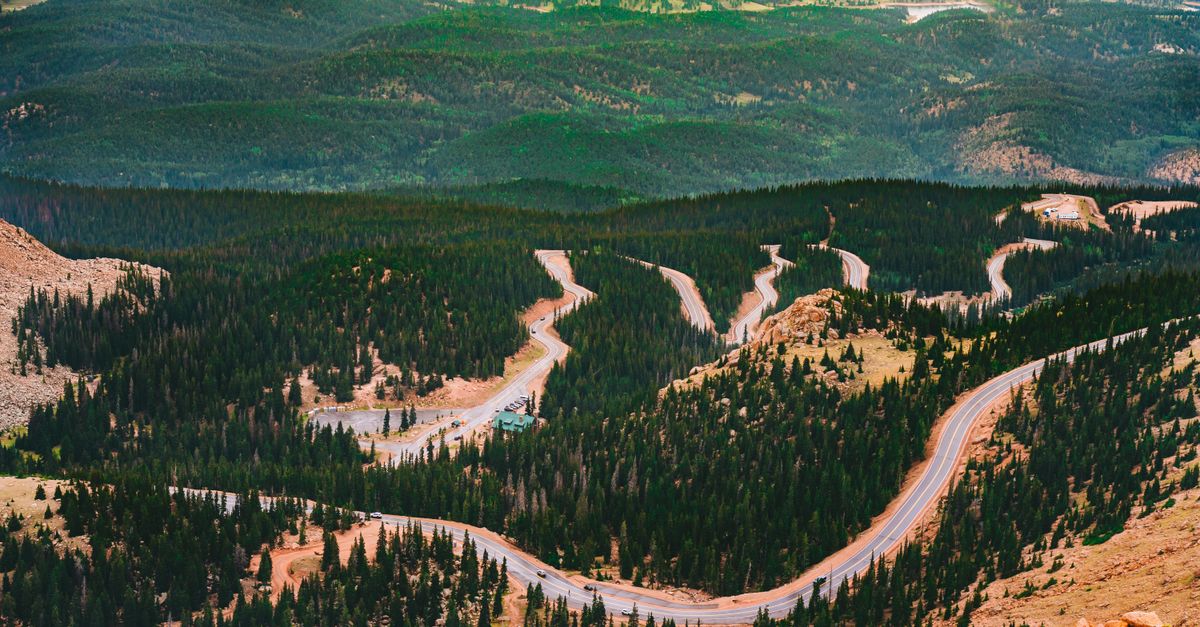 Aerial view of a winding road weaving through lush forested mountains, perfect for nature enthusiasts.