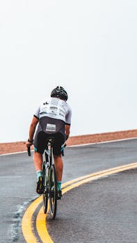 A cyclist riding uphill on a winding mountain road, seen from behind.