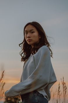 日落时分，一位年轻女子静静立于草地，展现出安宁与静谧