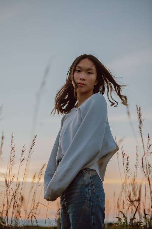 Free Young ethnic peaceful woman in sweater standing in dry grass Stock Photo