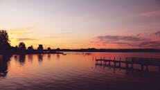 宁静的日落下，树木和码头的轮廓倒映在平静的湖面上