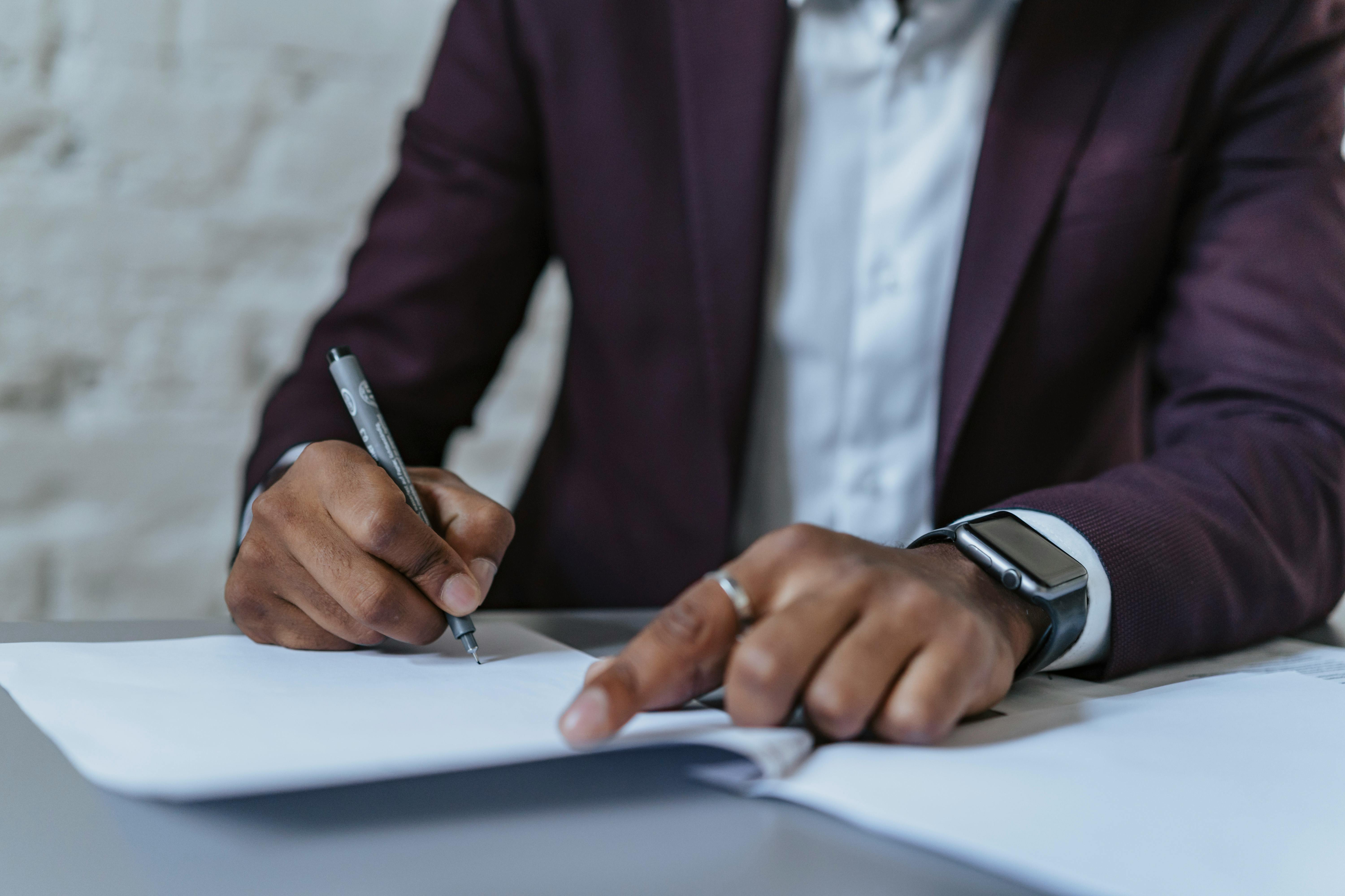 a man writing on white paper using a black pen