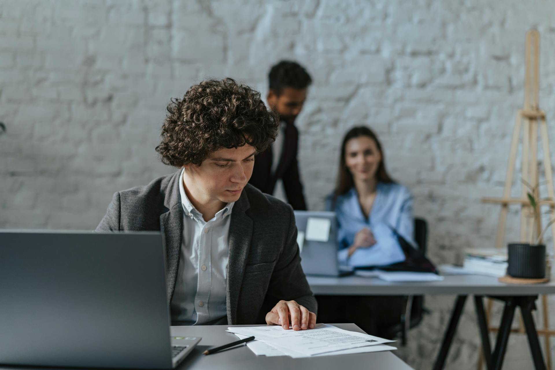 Business professionals working together in a modern office setting with focus on curly-haired man reviewing documents.