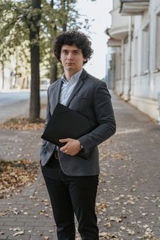 一位穿着西装的商业人士在绿树成荫的户外小路上拿着一份文件
