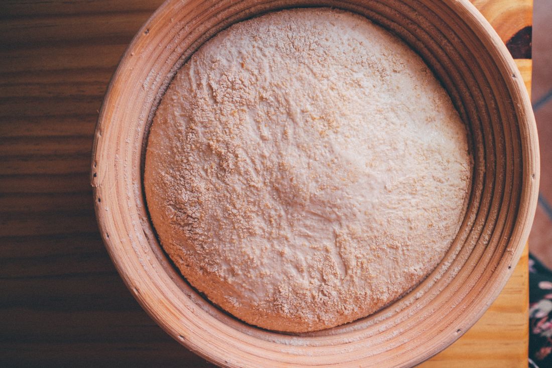 Round coiled rattan proofing basket holding floured bread dough from above