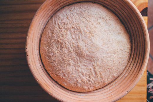 Round coiled rattan proofing basket holding floured bread dough from above