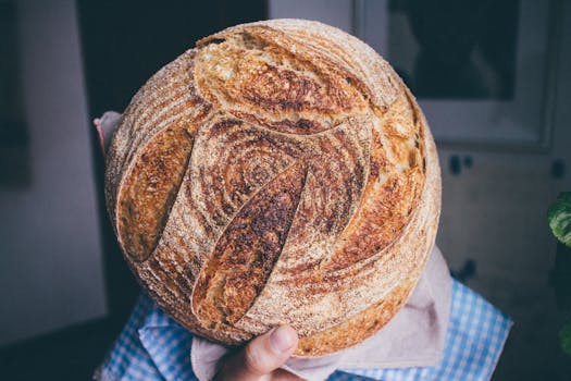 Freshly baked round sourdough bread held by hand, showcasing a rustic crust.