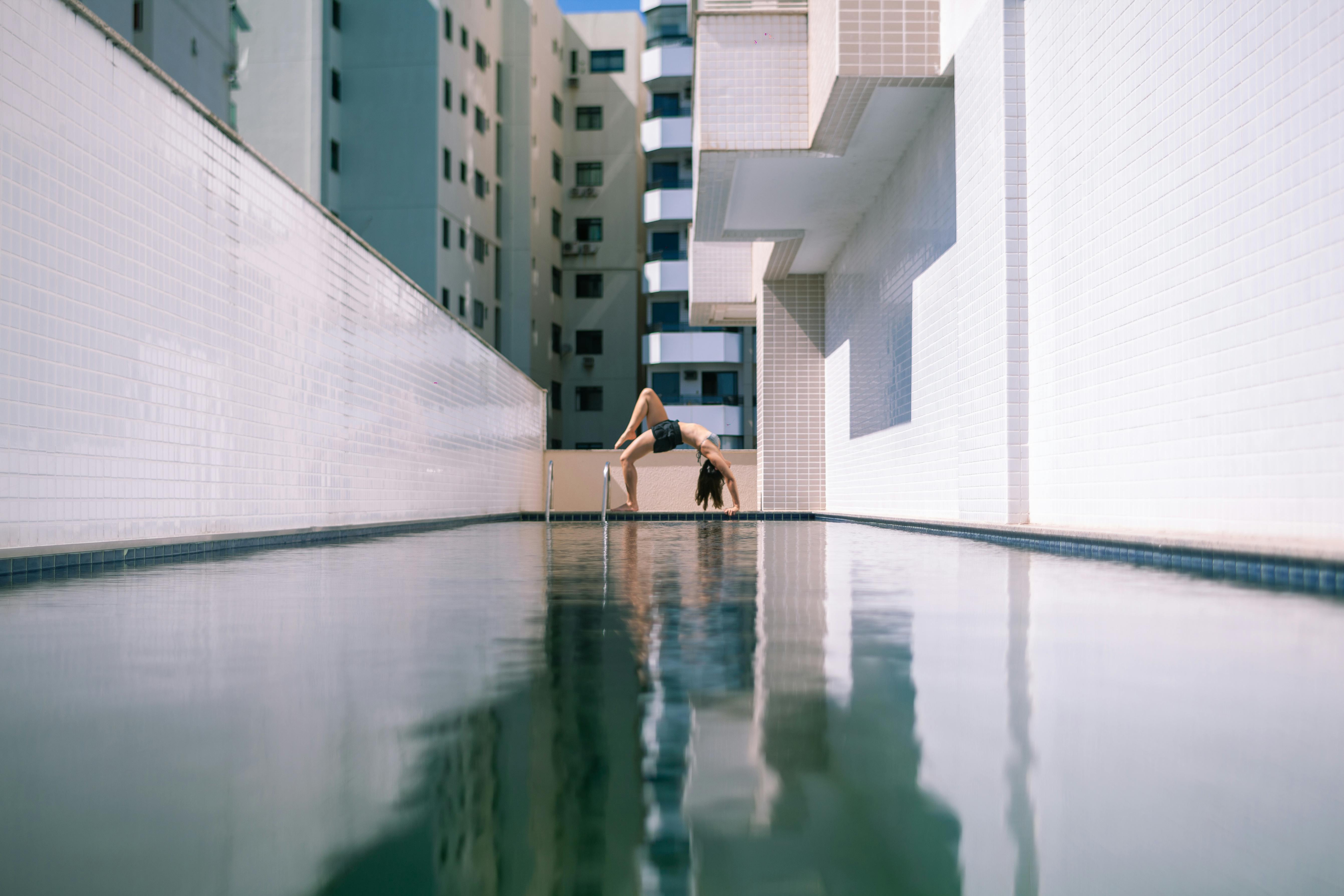 一名女子在城市游泳池旁练习瑜伽，摆出姿势，展现了身体的灵活性和现代生活方式