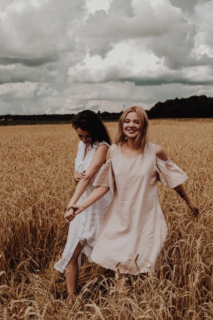Full body of young romantic women in summer dresses walking in meadow while holding hands