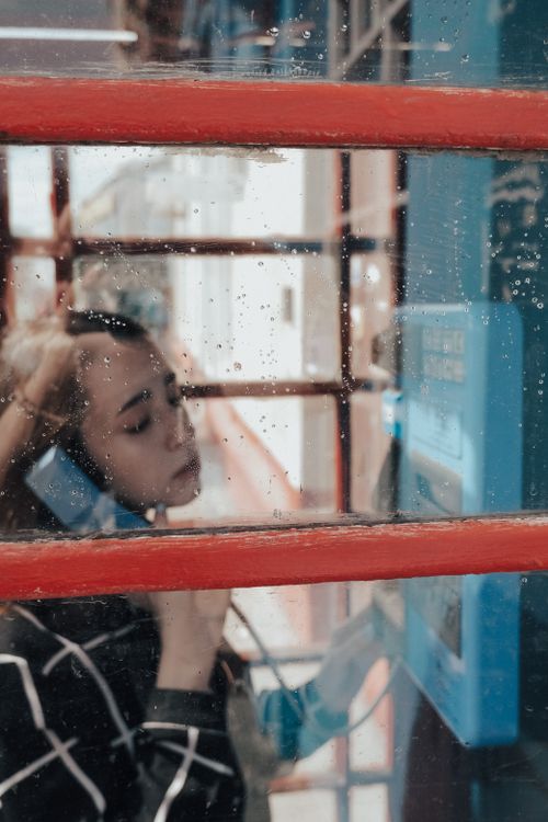 Free Brown haired female standing in urban phone box and holding bright blue handset while talking Stock Photo
