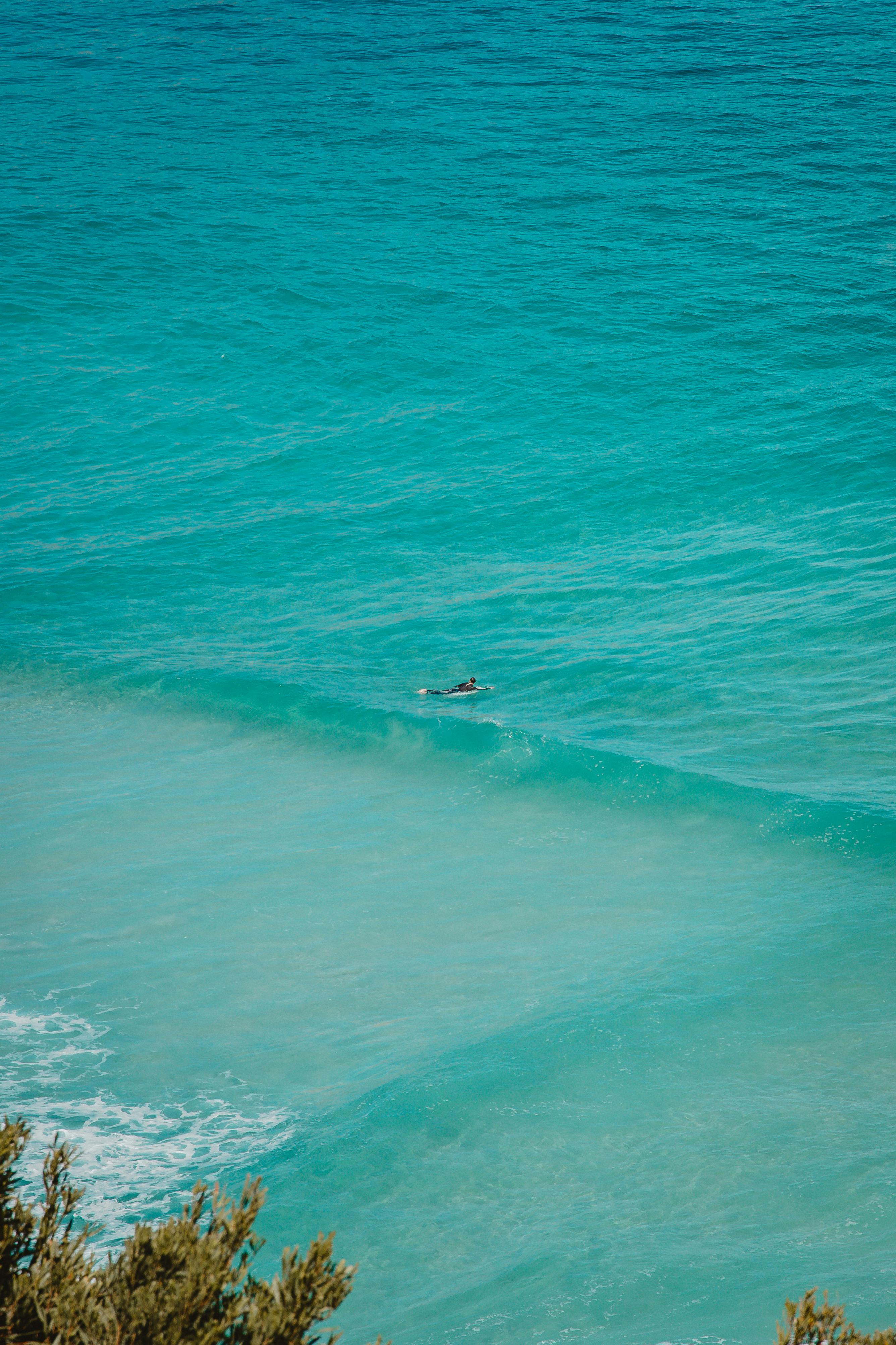 A lone surfer paddles in the vibrant turquoise waters, captured from above. Peaceful and scenic.
