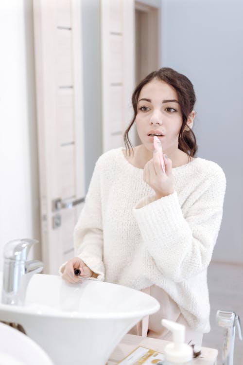 Woman in White Sweater Applying Lipstick   