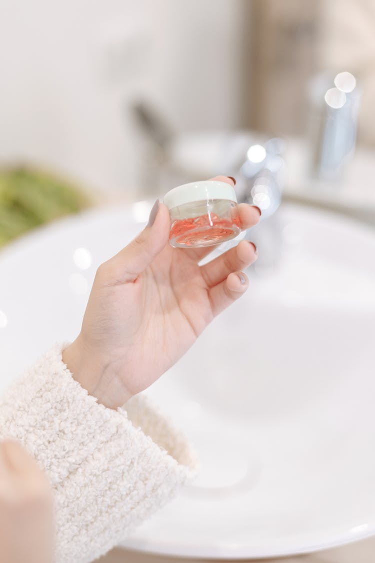 A Hand Holding A Small Container With Moisturizer