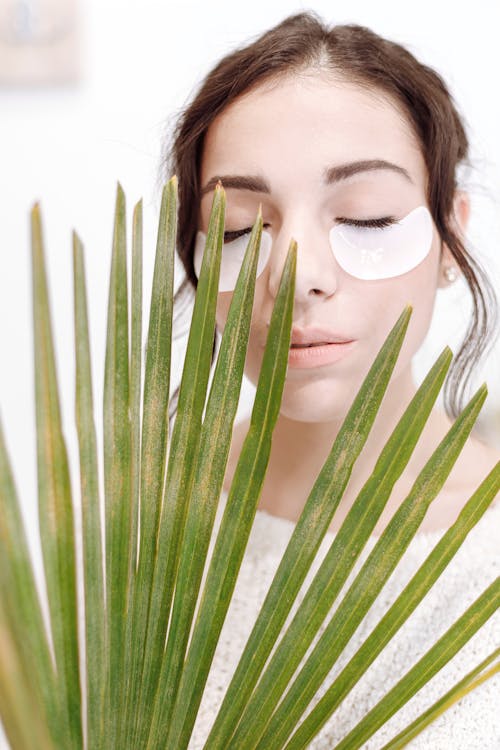 Woman with Under Eye Masks Standing Near Green Palm Leaf