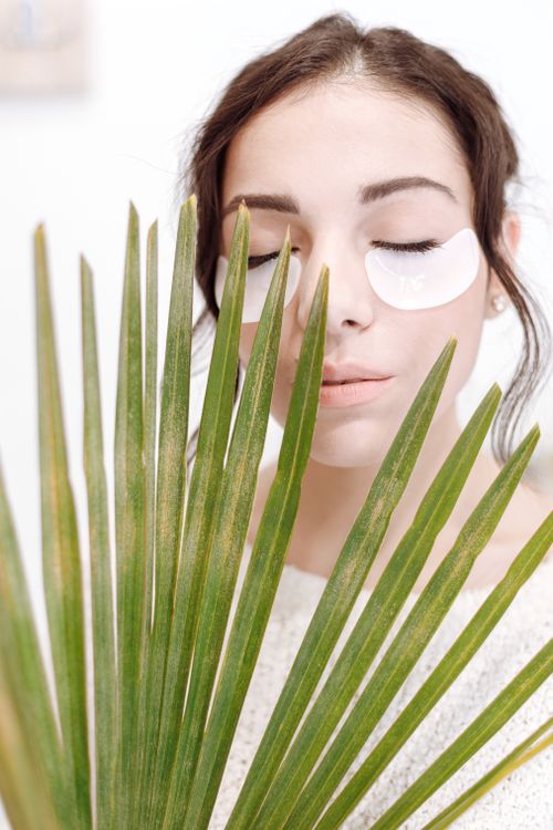Free Serene portrait of a woman relaxing with under eye masks and a palm leaf. Stock Photo