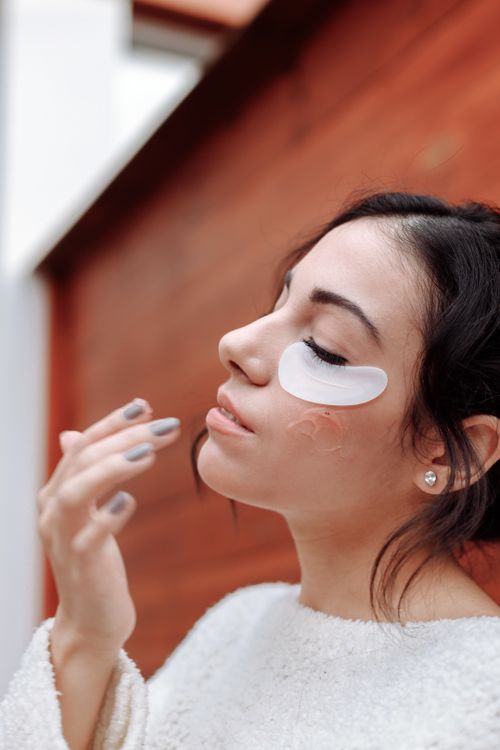 Free Woman applying a moisturizing under-eye patch for skincare treatment. Stock Photo