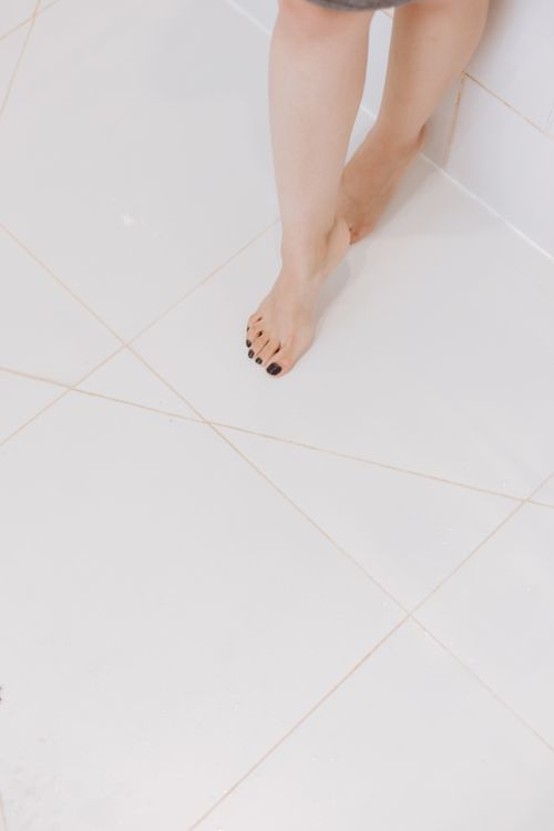 Free Close-up of barefoot woman with black manicured nails standing on a white tiled floor. Stock Photo