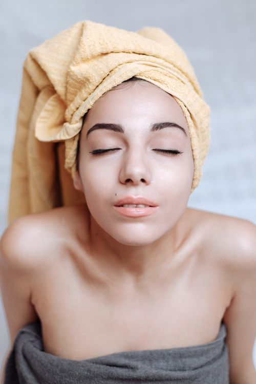 Free Portrait of a woman with eyes closed, wrapped in a towel, depicting relaxation and wellness. Stock Photo
