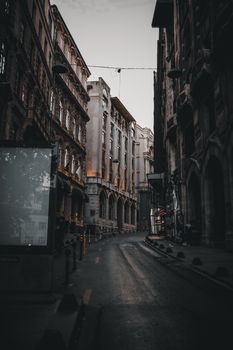 Narrow street with empty asphalt road surrounded with aged majestic buildings under gray sky