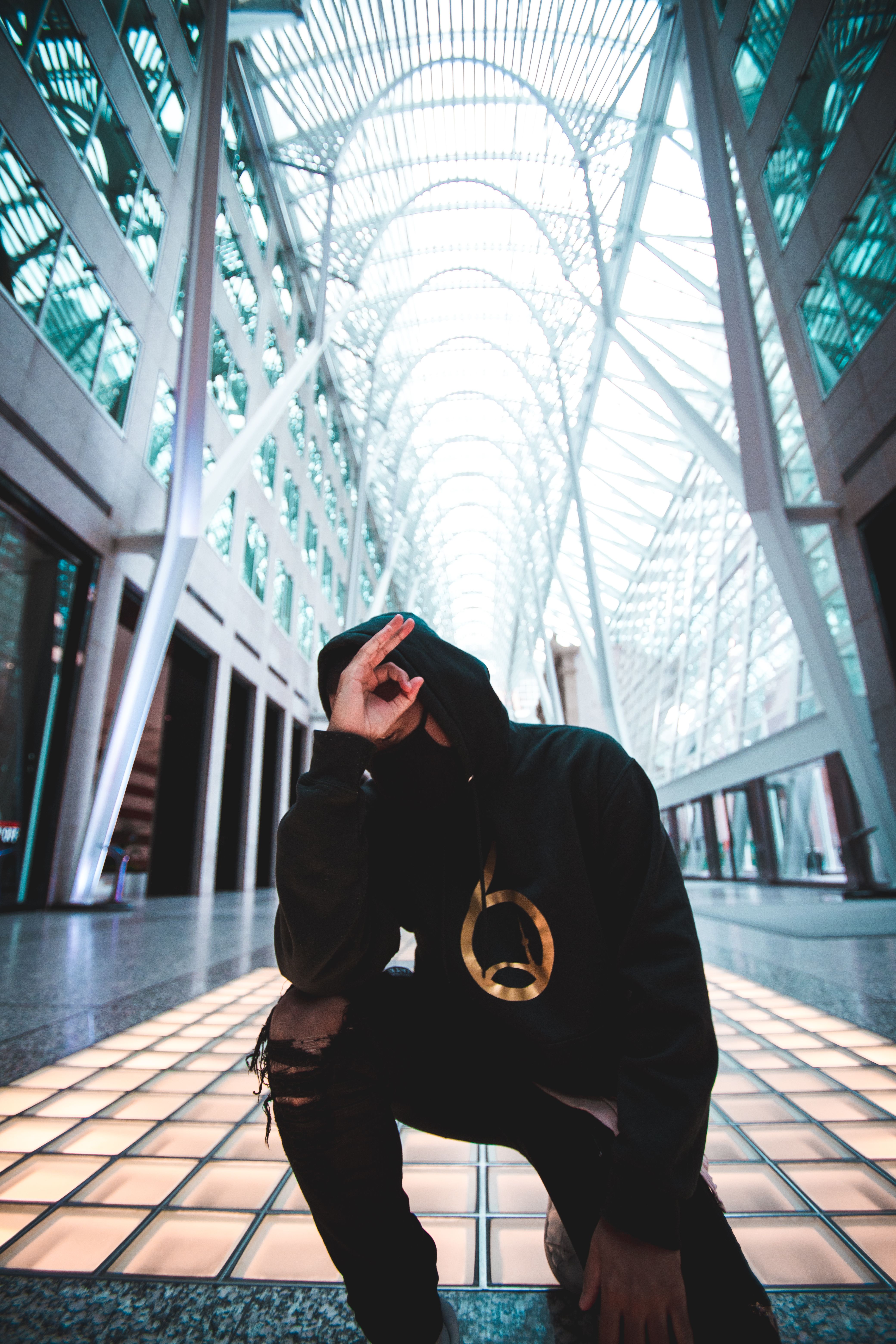 A person in a facemask and hoodie poses artistically in Toronto's modern architecture.