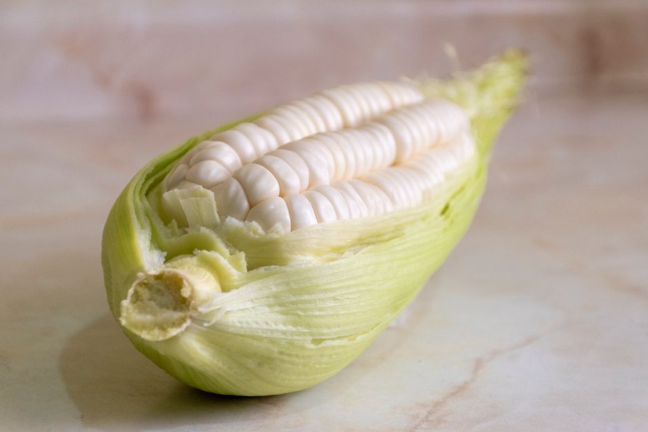 Large pale yellow choclo corn kernels served on the cob alongside fresh white cheese and avocado, a classic Ecuadorian plate.