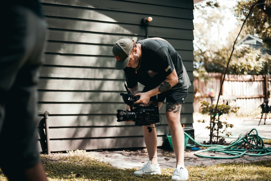 A videographer in casual attire filming outdoors with a professional camera. A videographer in casual attire filming outdoors with a professional camera.